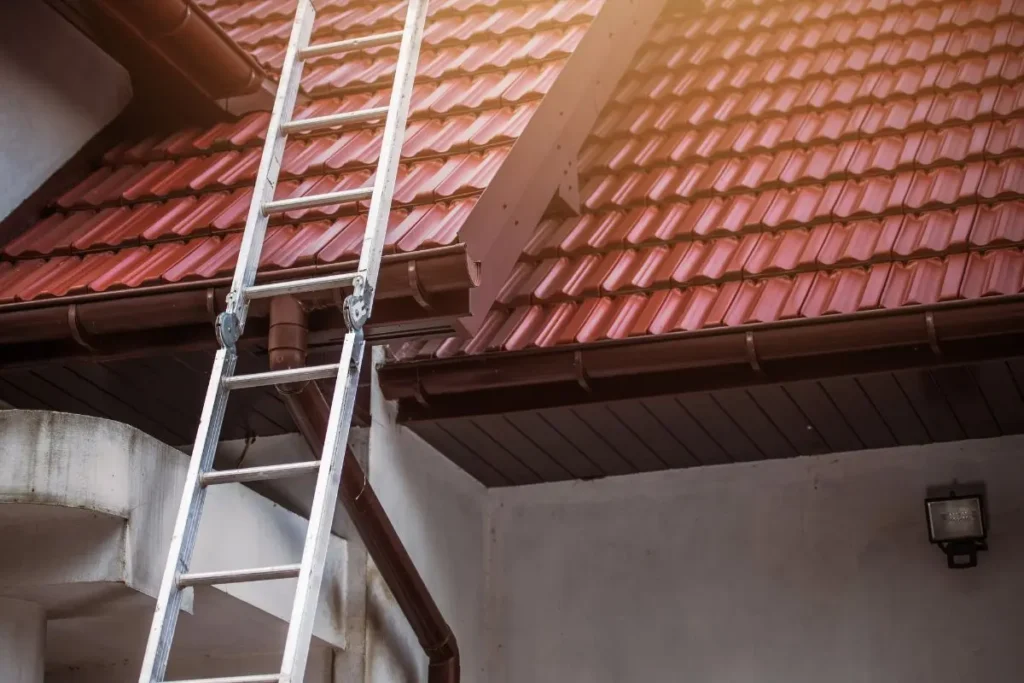 Échelle posée contre une toiture en tuiles rouges, rénovation de toiture