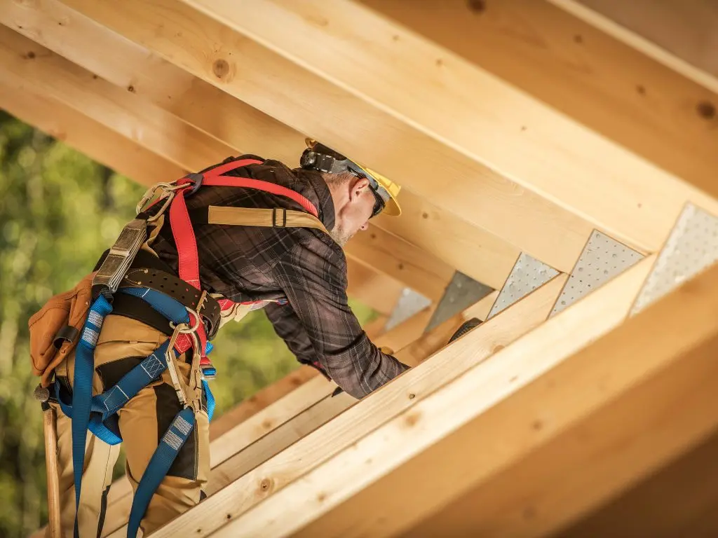 Charpentier avec harnais travaillant sur une charpente en bois, travaux de charpente