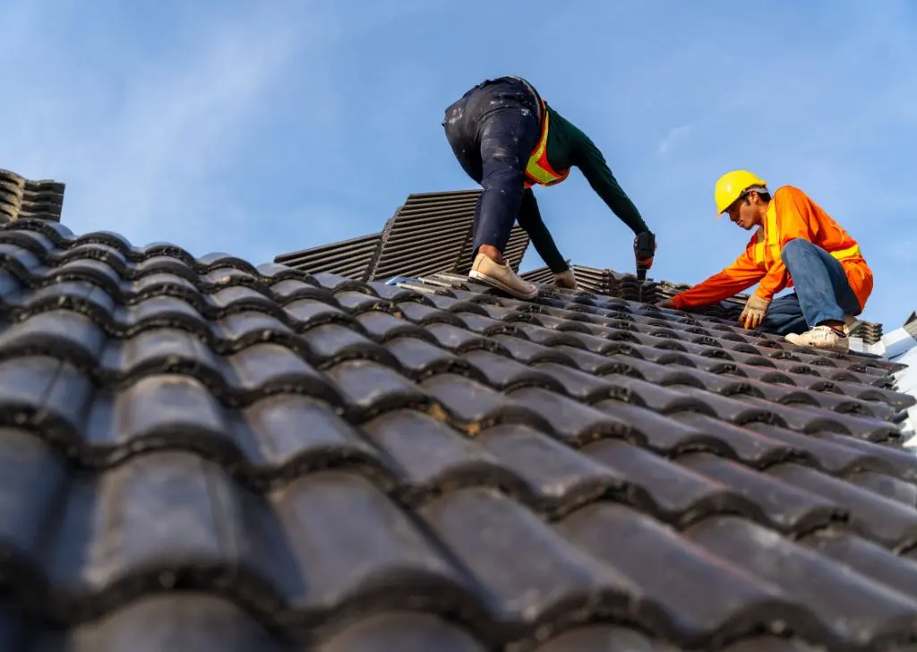 Deux couvreurs travaillant sur une toiture en tuiles sombres, réfection de toiture