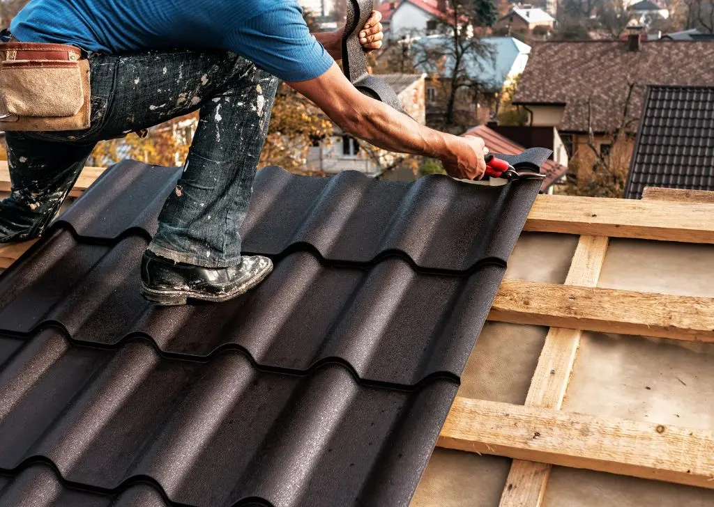 Couvreur posant des tuiles sombres sur des liteaux, réparation de toiture