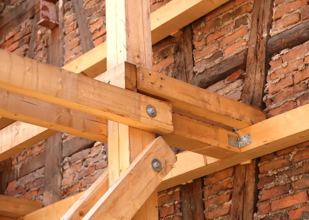 Charpente en bois neuf assemblée devant un mur en briques, traitement de charpente